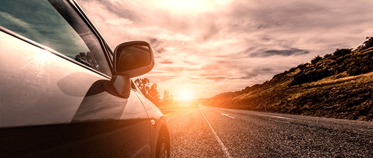 Banner Image of Car Driving Towards Sunset